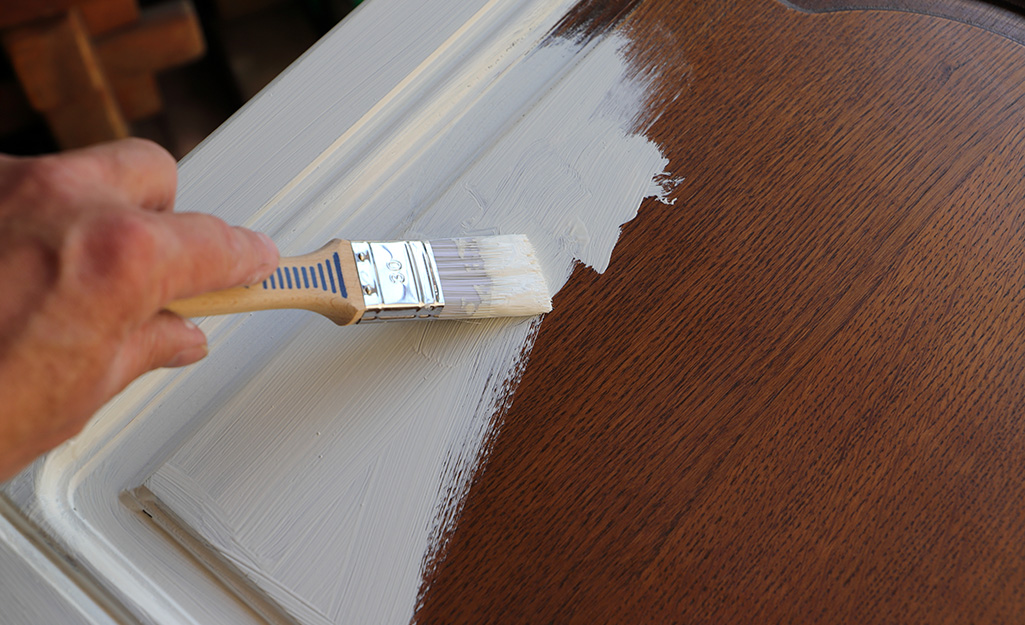 Someone brushes primer onto a wooden cabinet door.