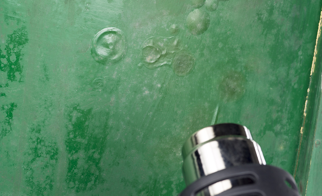 Someone uses a heat gun to strip green paint off a cabinet.