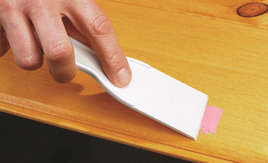 A person uses a putty knife to smooth out a patched cabinet hole.