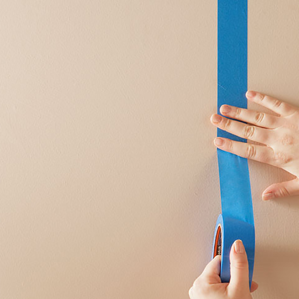 Hand applying a vertical stripe of painter's tape to wall