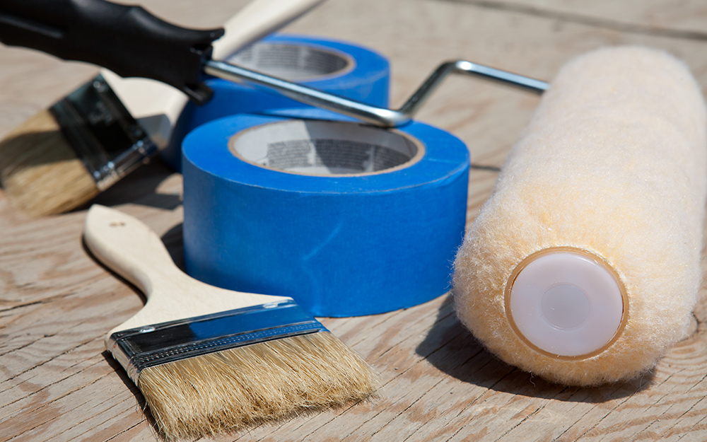 Painter's tape, brush and roller laying on a table.