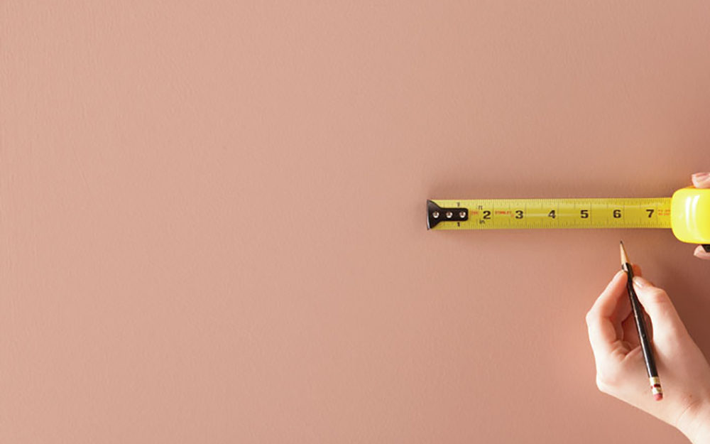 Hand using pencil and tape measure to mark and measure wall.