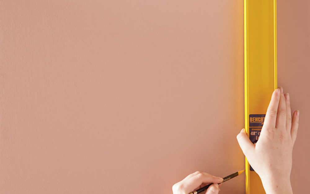 Hand using a level and pencil to mark a wall.