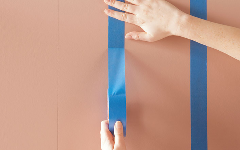 Hands applying painter's tape vertically to a wall.