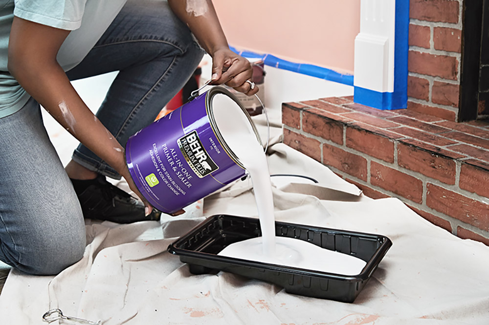 A person carefully pours paint into a pan before working on a room.