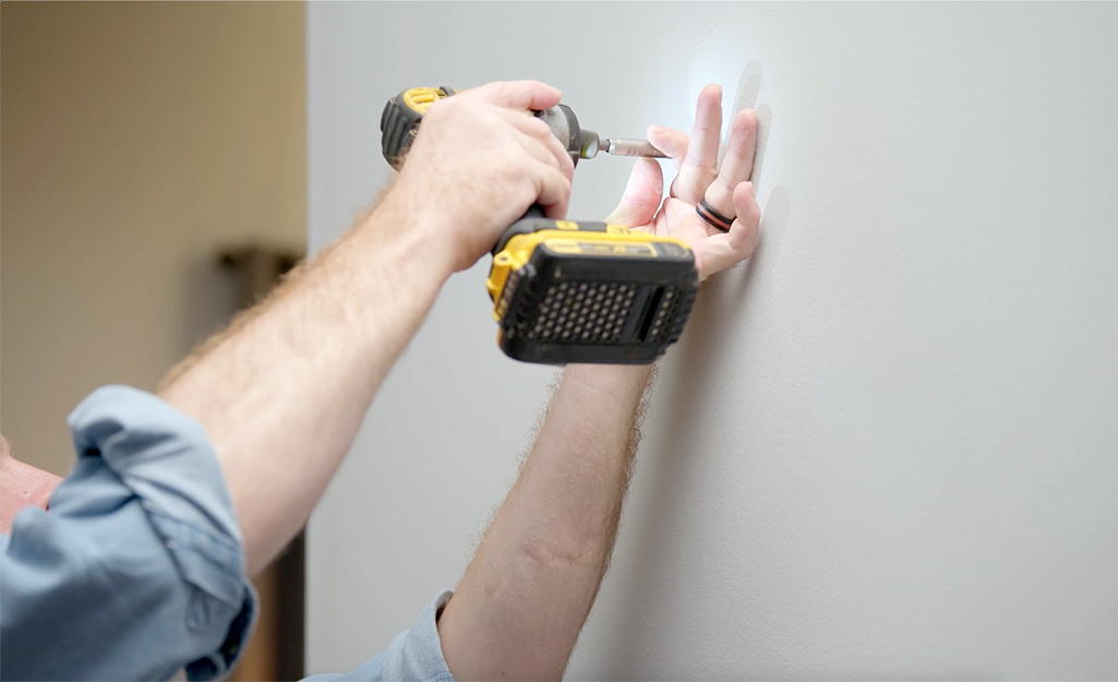 A person drills a hole in the wall to repair drywall.