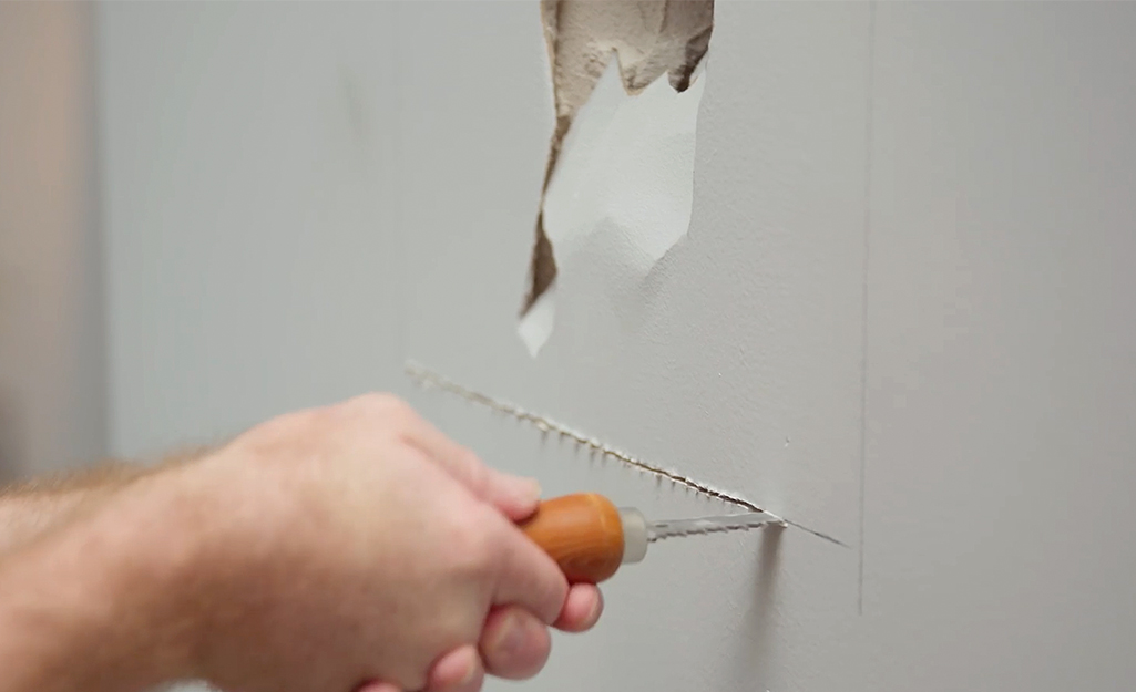 A person cuts around a large hole in drywall.
