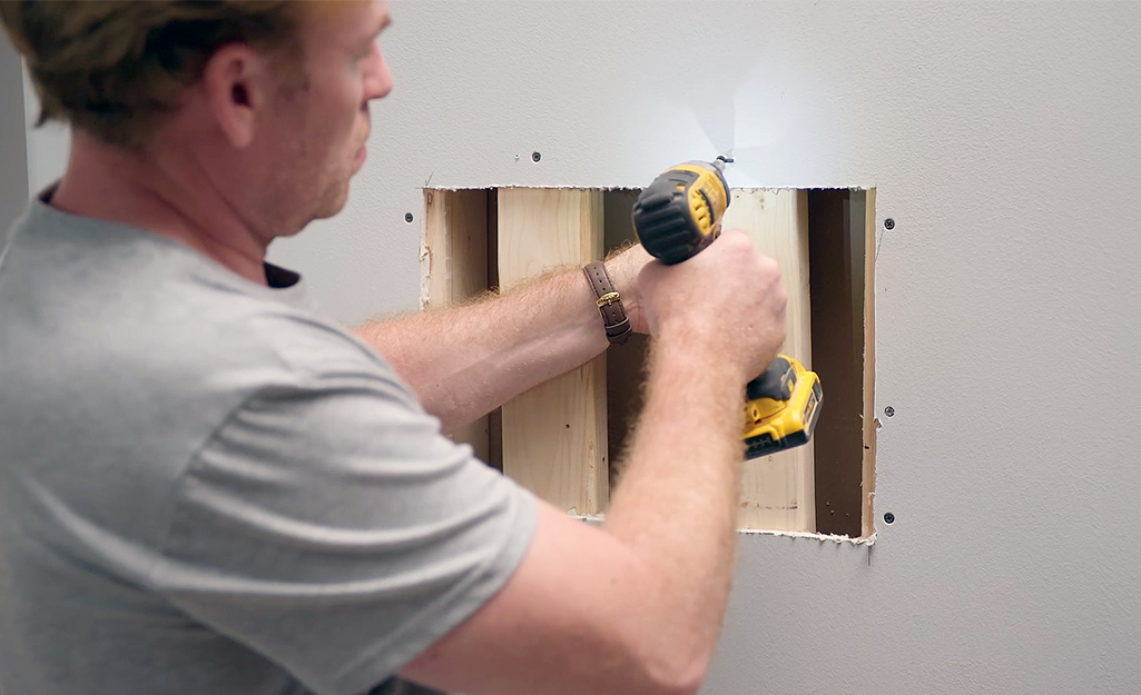 A person installs support behind drywall.