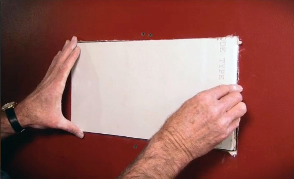 A person fitting a drywall patch into a wall.