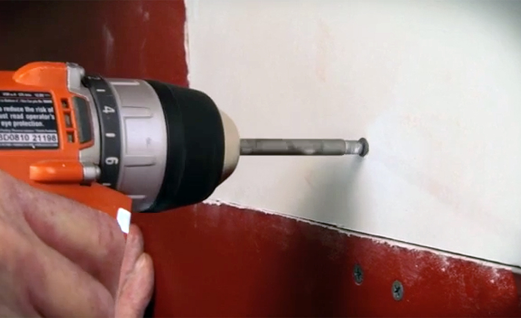 A person drilling a drywall screw into a drywall patch in the wall.