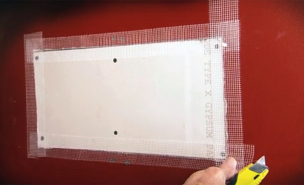 A person sealing drywall patch seams with drywall joint tape.