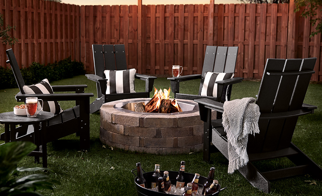 A brick fire pit with Adirondack chairs in a backyard.