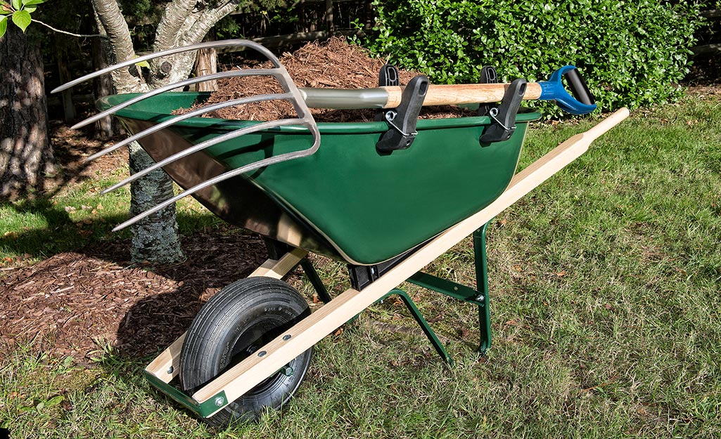 A pitchfork laying atop a wheelbarrow.