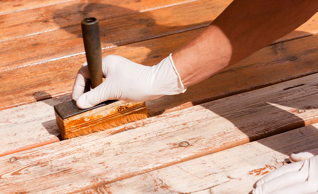 A person running a paintbrush between two deck boards.