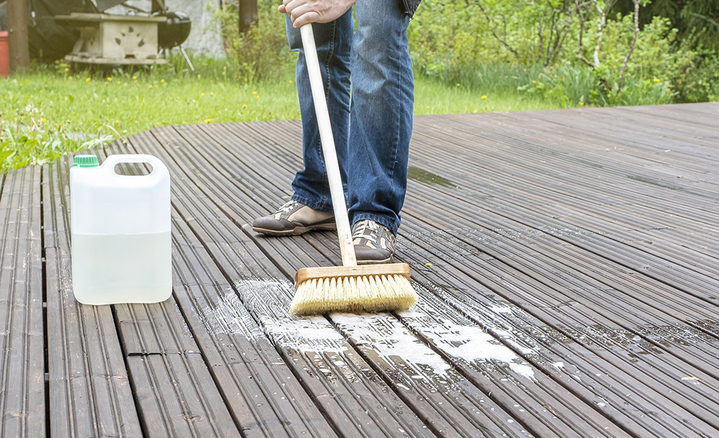 A person scrubbing a deck with a broom.