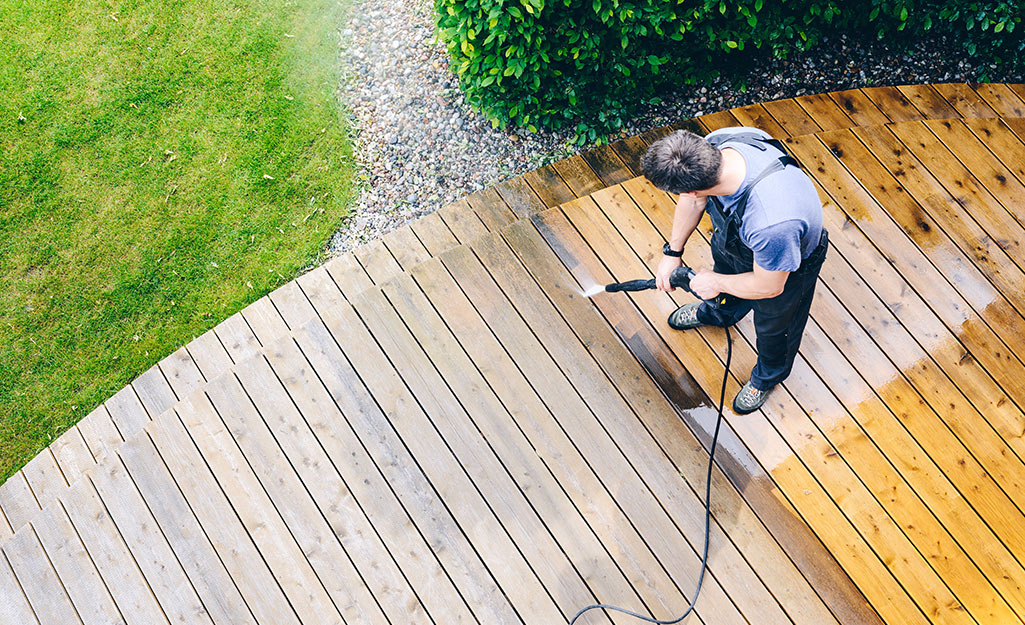 A person pressure washing a deck.