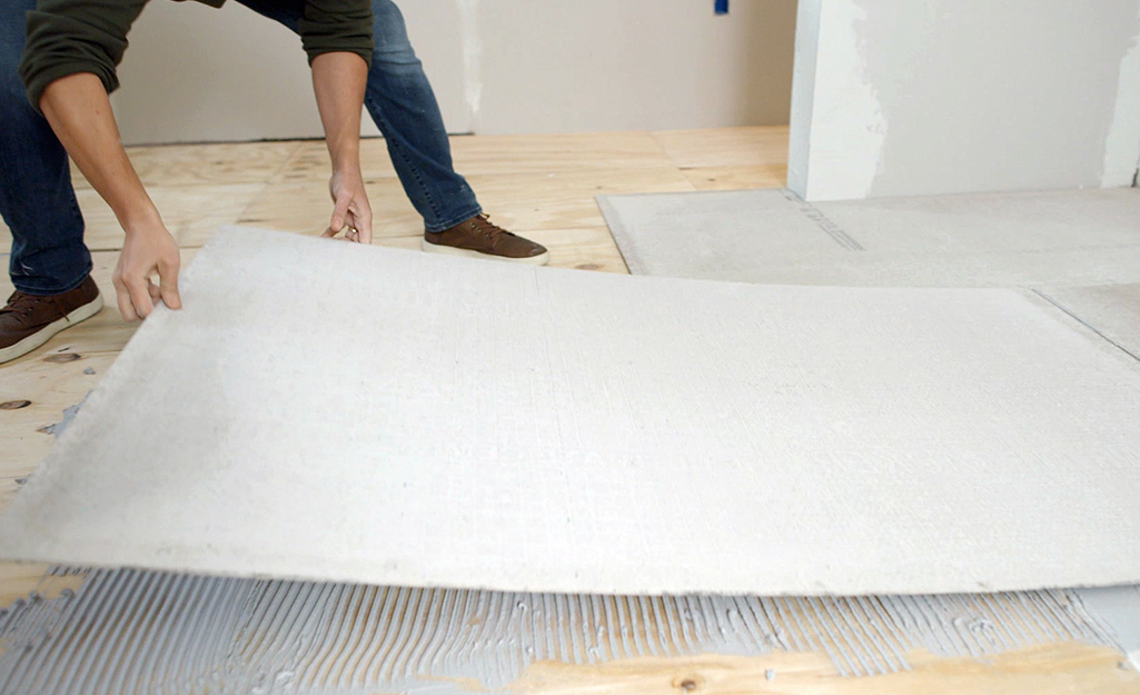 A man places a piece of backer board on thin-set that has been spread on a wood subfloor.