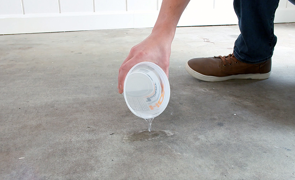 A man pours water from a small white container onto a concrete subfloor.