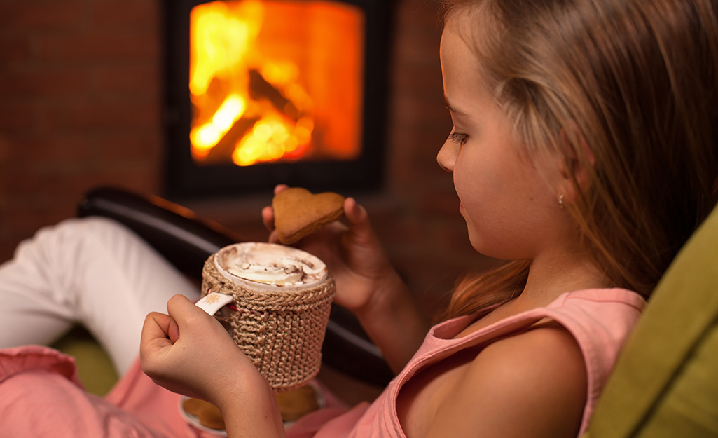 A child snuggling by a roaring fire with a cup of cocoa.