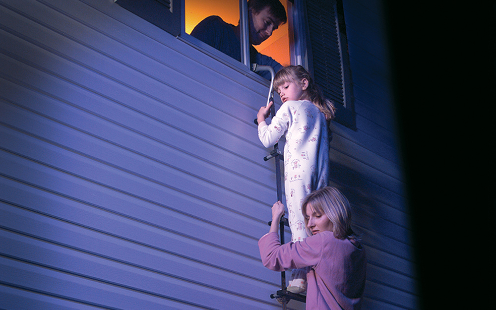 Family members hang onto a second floor fire escape ladder.