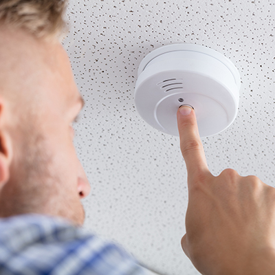 A person tests a smoke alarm on the ceiling.