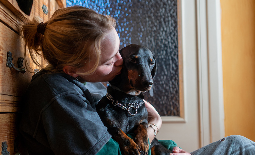 Woman sitting with dog in bathroom.