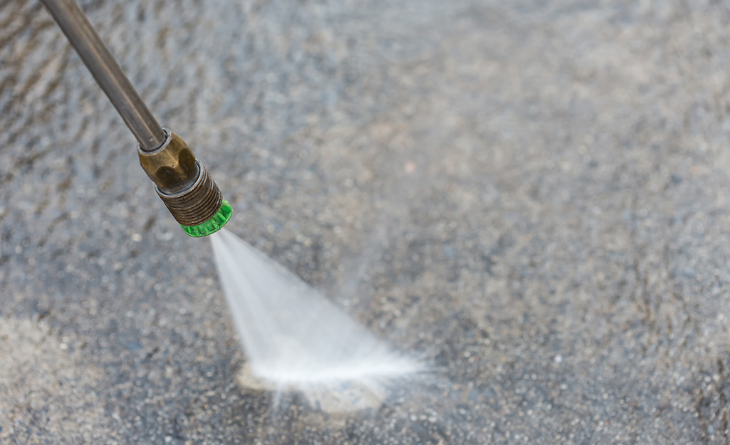 Water comes out of the nozzle of a pressure washer and hits a concrete driveway in this detail shot.