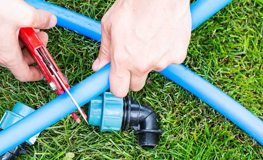 A person cutting a garden hose with shears.