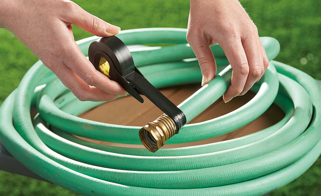 A person taping a garden hose with black tape.