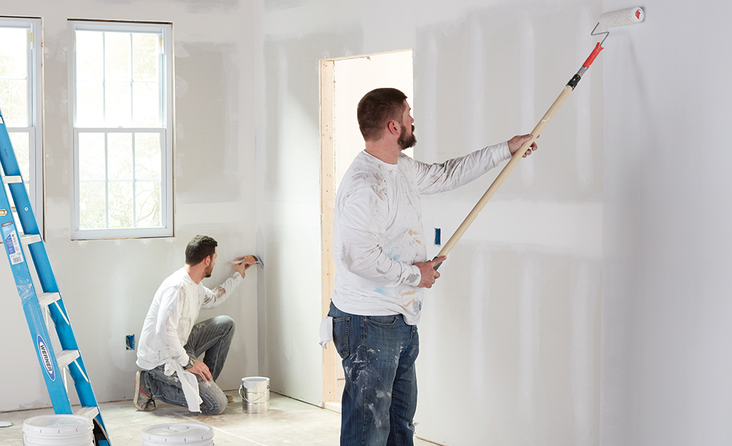 Two people applying a coat of primer to an unfinished wall.