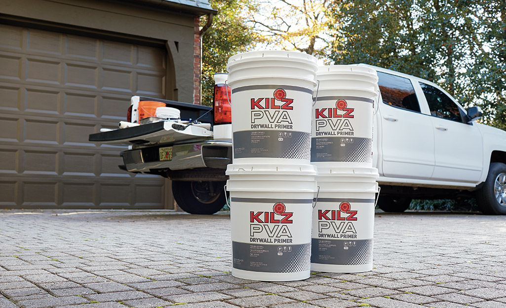 Four buckets of primer placed on a driveway next to a pickup truck.