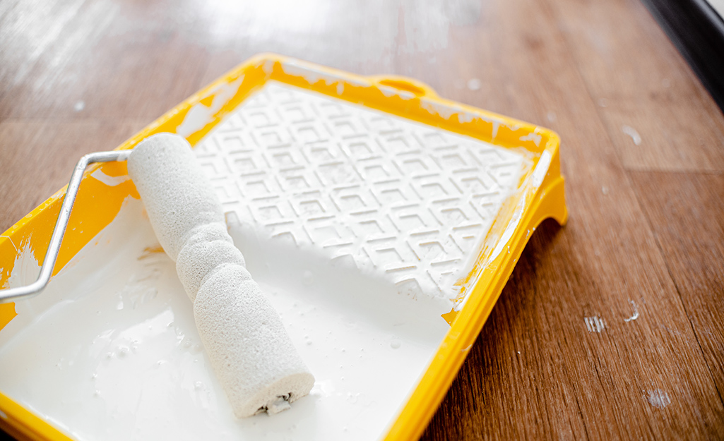 A paint roller resting in a paint tray with primer.