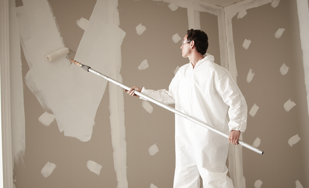 A person using a paint roller on an extension pole to apply primer to an unfinished wall.