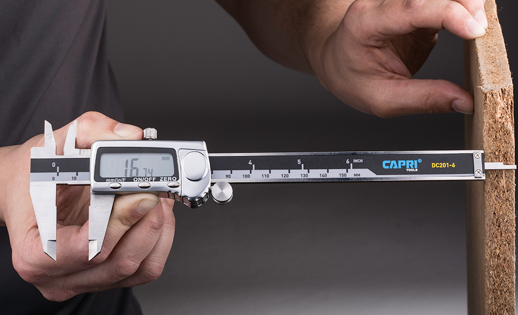 A person uses digital calipers to measure the depth of a board.