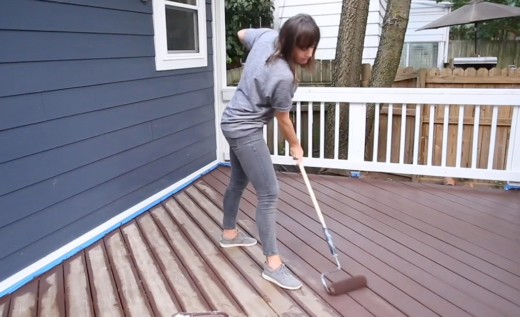 A person applies stain to a deck with a paint roller