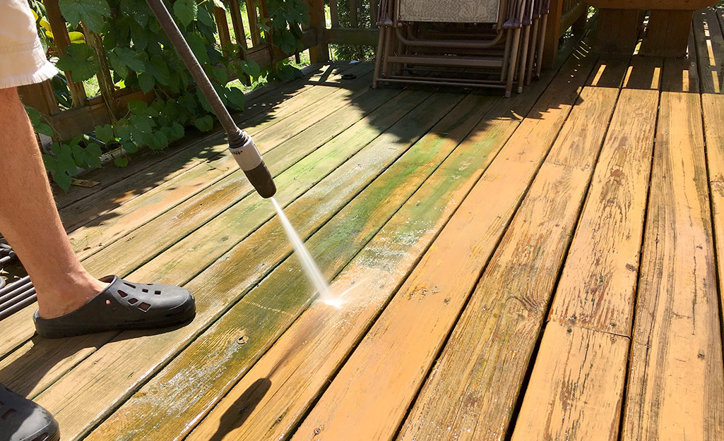 A person cleans a deck with a pressure washer.