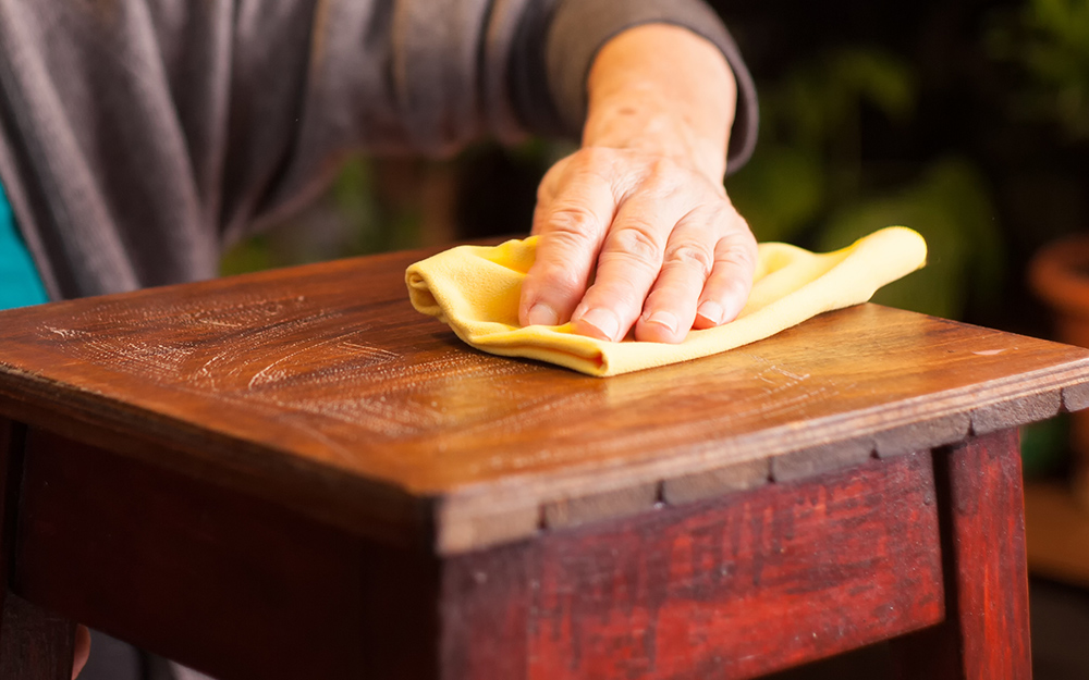 A person wiping the top of a piece of furniture.
