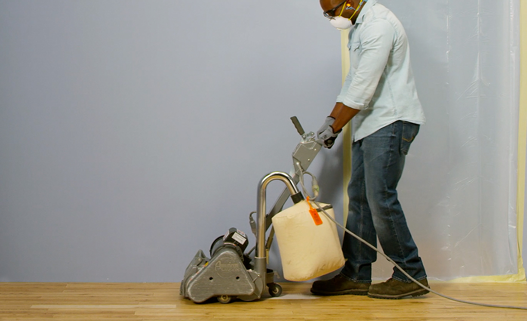 A person uses a drum sander on hardwood floor.