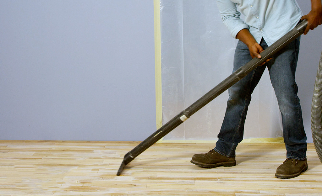 A person vacuums the dust from a hardwood floor.