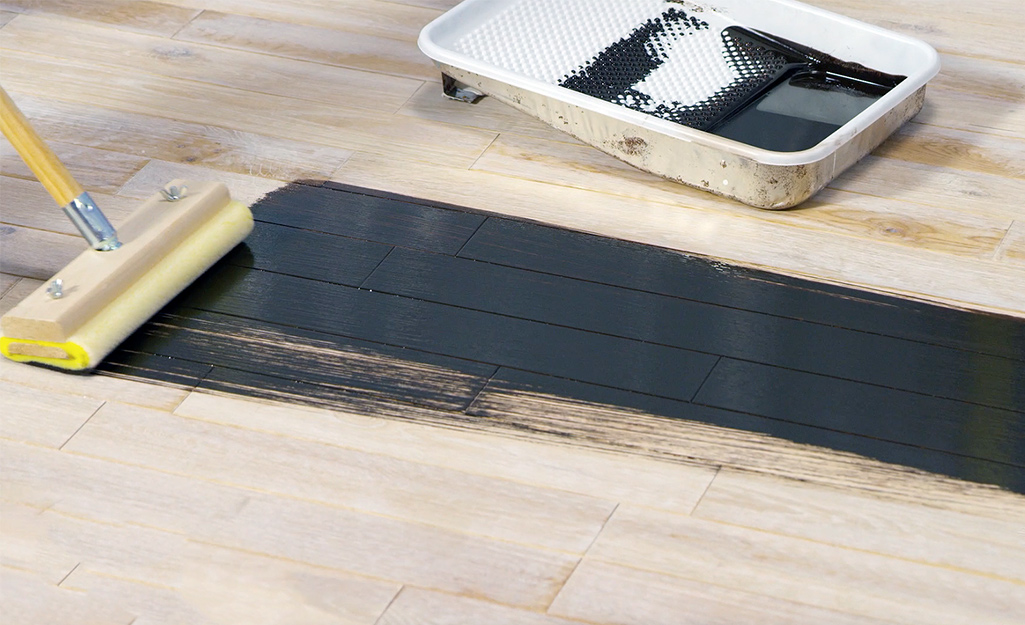 A person applies a finish to a hardwood floor with a brush.