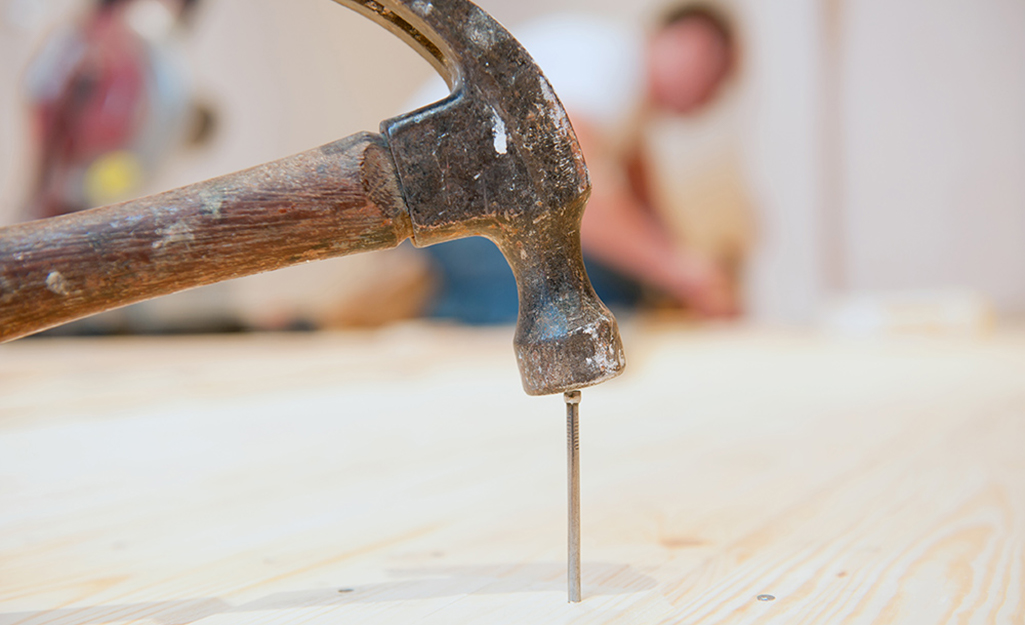 A person secures a loose floorboard with a hammer and nail.