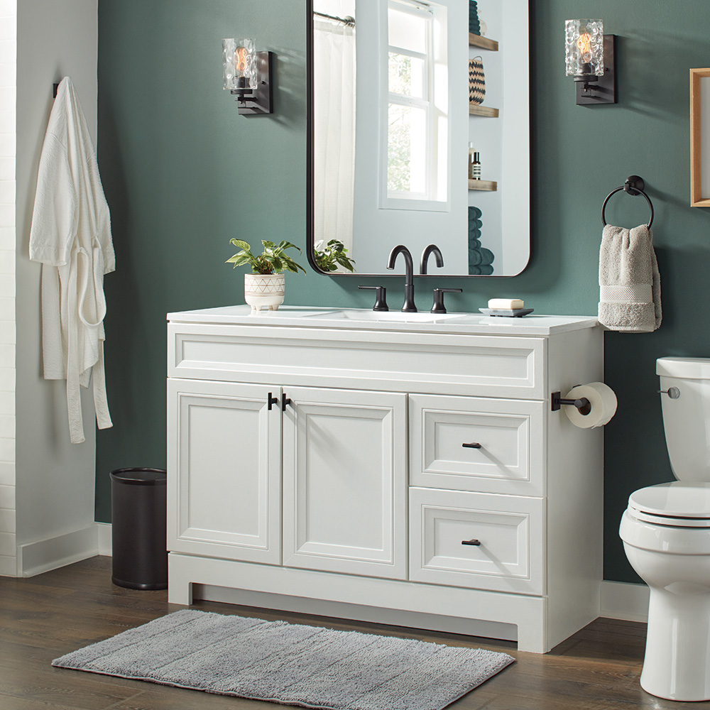 A white bathroom vanity stands in front of a green wall and next to a toilet.