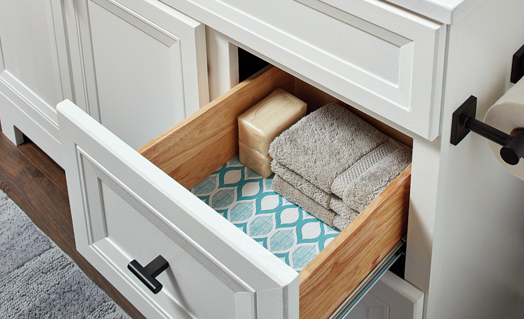 An open drawer in a bathroom vanity shows folded washcloths, bars of soap and diamond patterned contact paper.