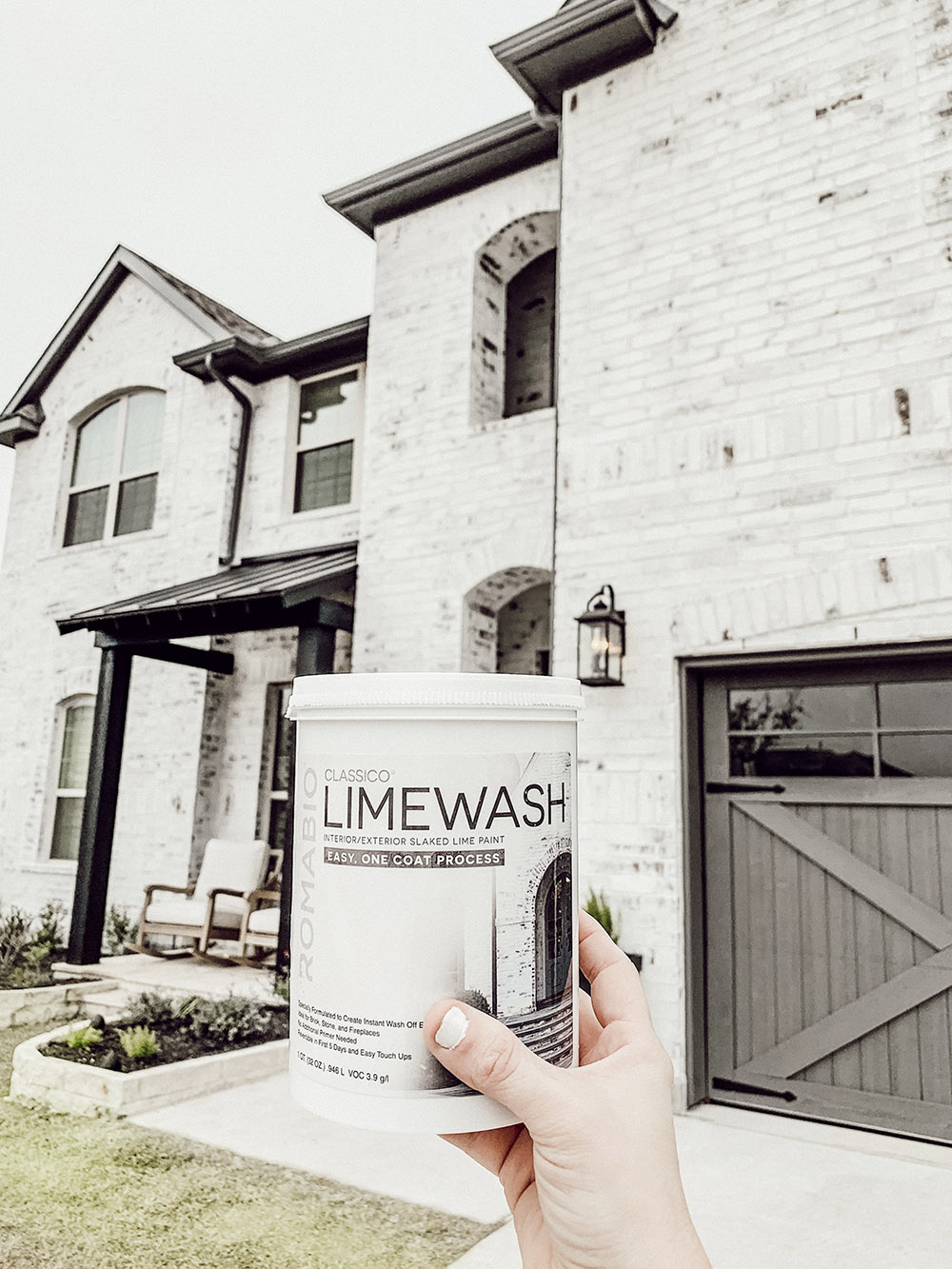 A person holding a can of classico limewash in front of a home.