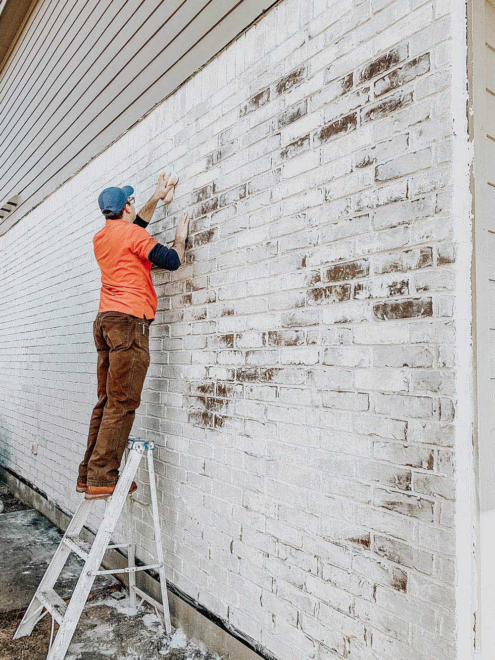 A man standing on a ladder applies classico limewash to a home's exterior.