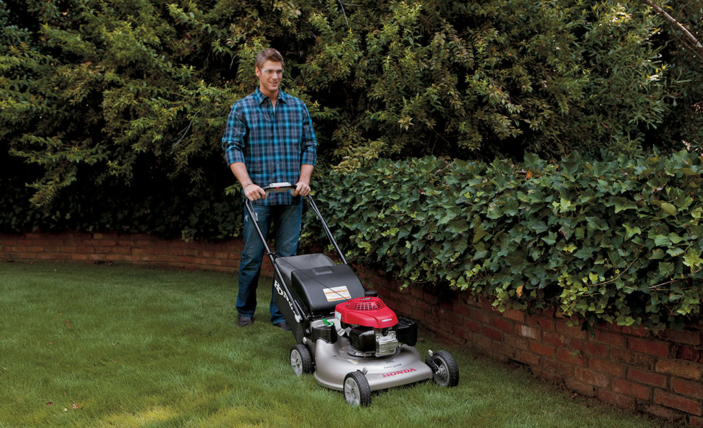 A gardener pushes a lawn mower over a green lawn.