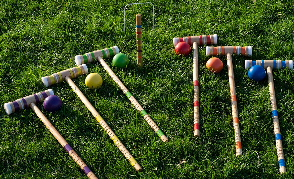 Croquet mallets, balls and a wicket in a green lawn.