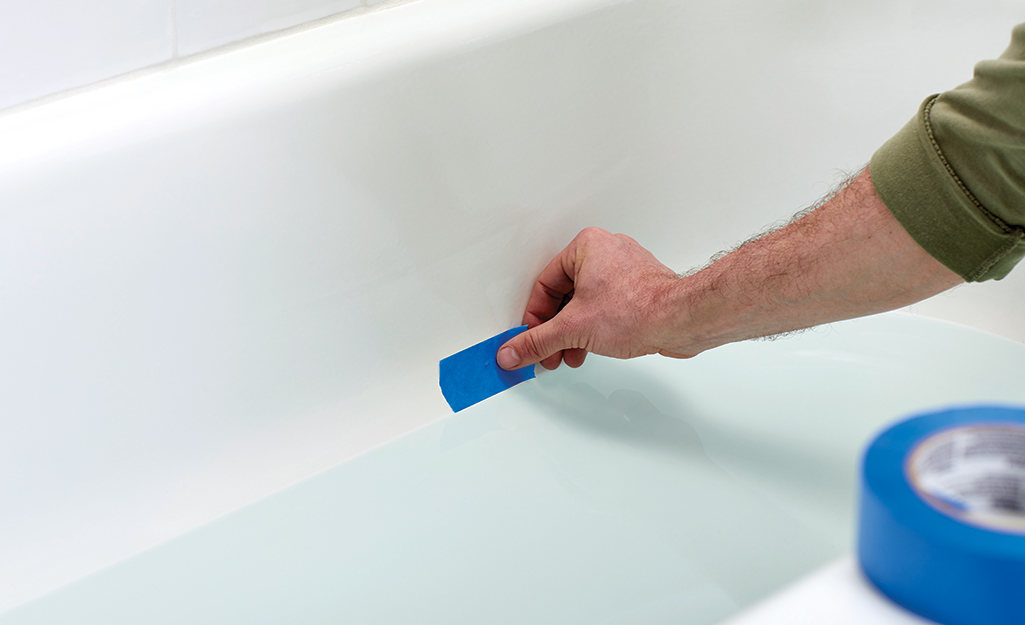 A person uses blue painter's tape to mark the water level in a tub
