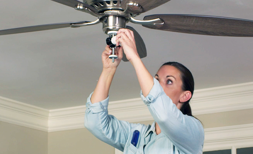 A person removes a lightbulb from a ceiling fan.