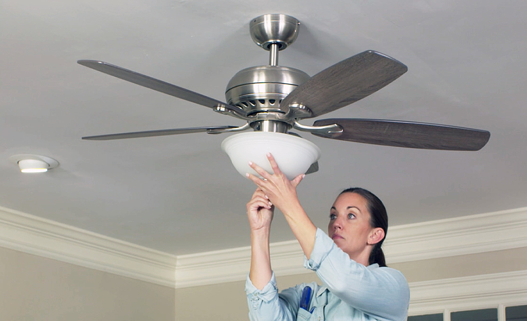 A person removes the light kit from a ceiling fan.